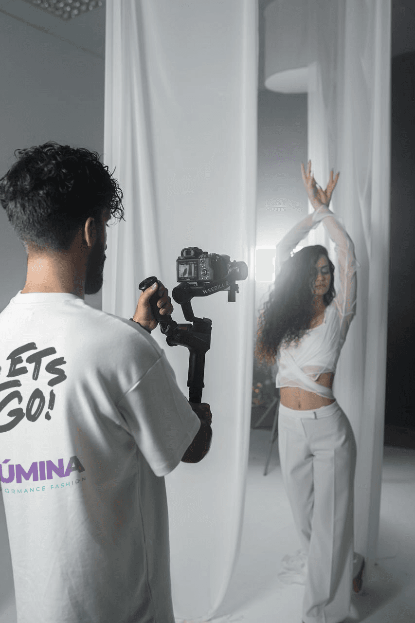 Bastidor de gravação: videomaker da Lúmina filma uma modelo de look branco no estúdio.